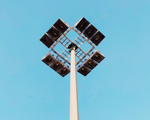 Poteau d'éclairage en métal avec plusieurs projecteurs, fond de ciel bleu.
